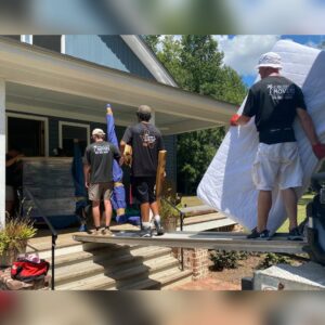 Jubilee City Movers team members carrying a mattress and wrapped items from a house to a moving truck in Montgomery, AL.