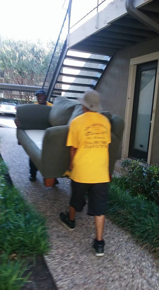 Two Ang Moving Co movers carrying a sofa along a pathway in Dallas, TX