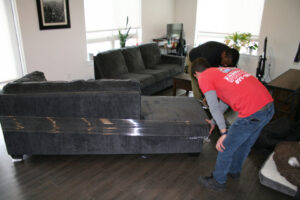 Two movers carrying a wrapped sofa into a home for Fatboy Slims Moving Company in Colorado Springs, CO.