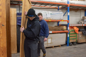 Two movers from N. L. Wilson Moving and Storage carrying a large wooden panel in a warehouse in Olathe, KS.