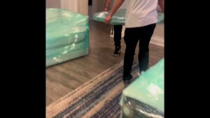 Two movers from Gifted Journey Movers carrying a large, wrapped piece of furniture down a hallway in Gulfport, MS.