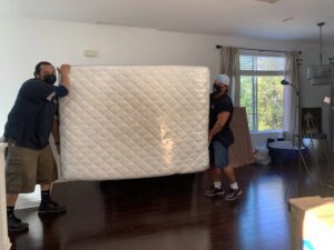 Two movers from Cheap Movers Los Angeles carefully carrying a large, plastic-wrapped mattress inside a house in Los Angeles, CA.