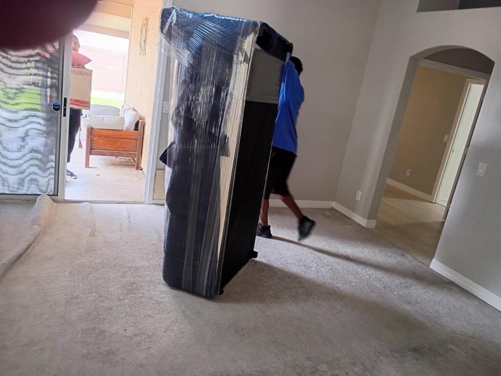 Two professional movers carrying a large, wrapped sofa into a house for Az Student Movers in Scottsdale, AZ
