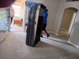 Two professional movers carrying a large, wrapped sofa into a house for Az Student Movers in Scottsdale, AZ