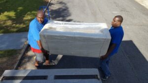 Two Ron's Moving team members carrying a wrapped sofa onto a moving truck ramp in Little Rock, AR.