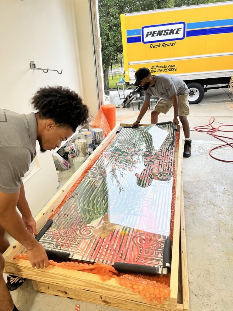 Two movers from Gifted Journey Movers carefully crating a large piece of artwork for safe transport in Gulfport, MS.