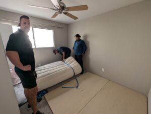 Three professional movers handling a rolled-up mattress in a bedroom for Az Student Movers in Scottsdale, AZ