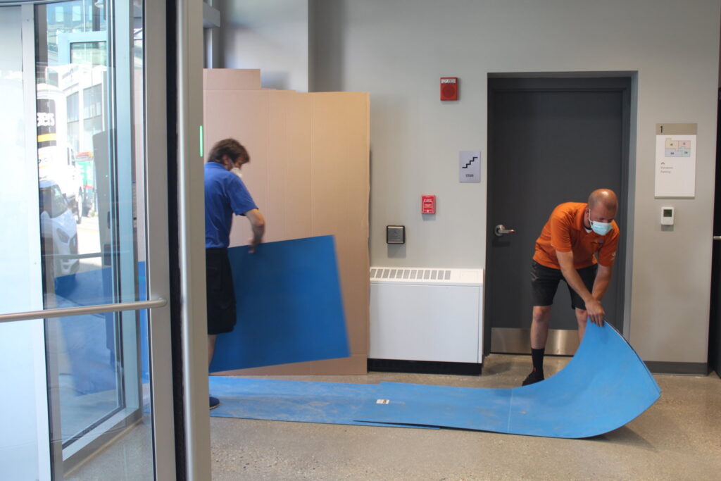 Two movers laying down blue floor protection mats for Coakley Brothers & Brothers Interiors in Milwaukee, WI.
