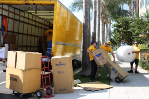 Movers from Sunshine Moving Services LLC loading moving boxes and a large roll of bubble wrap onto a truck in San Diego, CA.