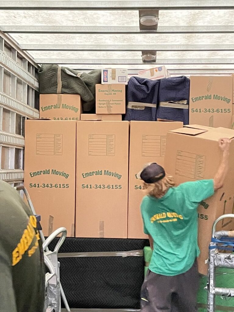 Movers from Emerald Moving & Storage, Inc. efficiently loading branded boxes into a moving truck in Eugene, OR.