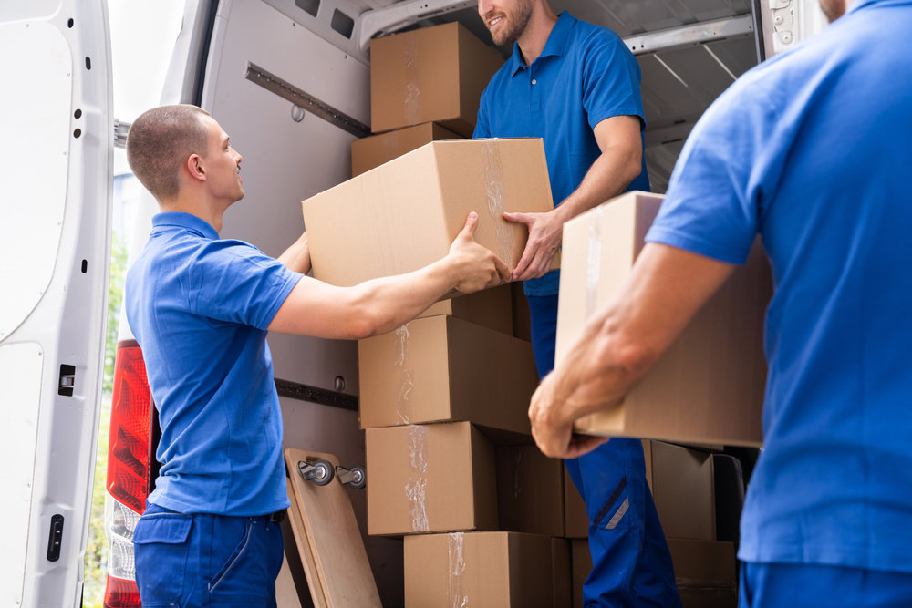 Three professional movers from Three Movers in Henderson, NV, loading cardboard boxes into a moving van.