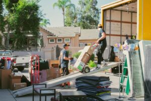 Two movers from Sunshine Moving Services LLC efficiently loading moving boxes onto a truck using a ramp in San Diego, CA.