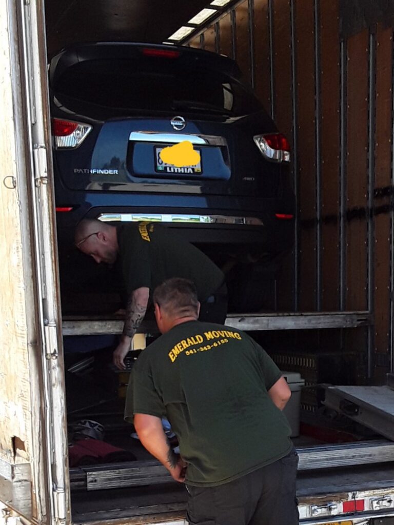 Two movers from Emerald Moving & Storage, Inc. loading a car and other items into a moving truck in Eugene, OR.