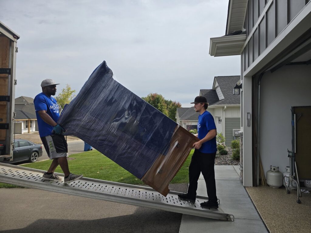 Two movers loading a large, wrapped dresser up a ramp into a moving truck for Goal Line Moving in Maple Grove, MN.