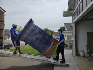 Two movers loading a large, wrapped dresser up a ramp into a moving truck for Goal Line Moving in Maple Grove, MN.