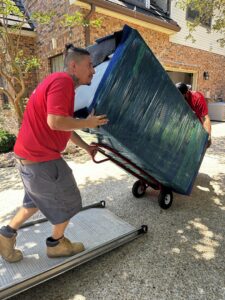 Professional movers loading a large, wrapped furniture item onto a moving truck using a dolly for Packsen Moving in San Antonio, TX.