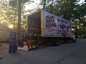 Movers loading wrapped furniture onto a Ron's Moving truck with a ramp and dolly in Little Rock, AR.