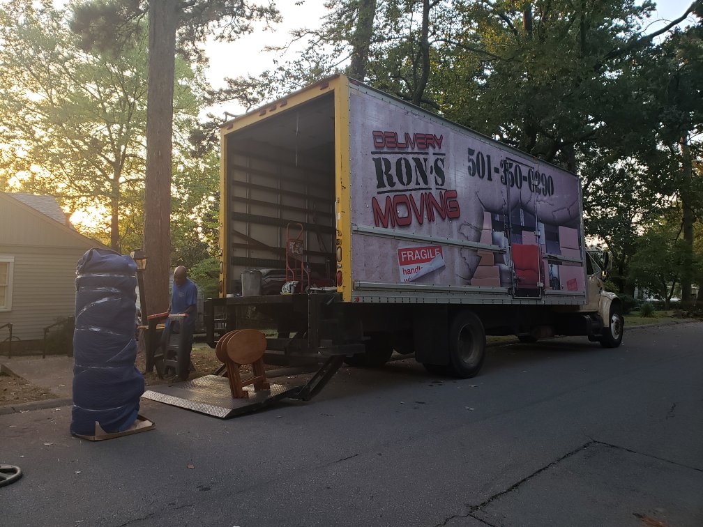 Movers loading wrapped furniture onto a Ron's Moving truck with a ramp and dolly in Little Rock, AR.