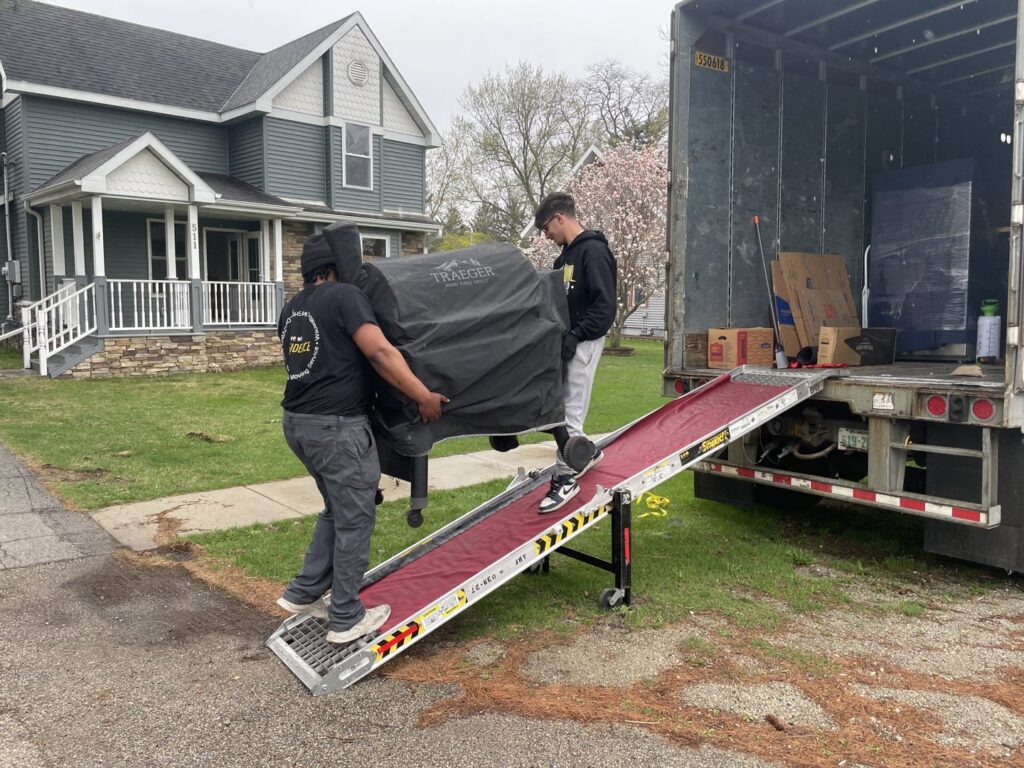 Shield Moving Services movers loading a large grill onto a moving truck using a ramp in Milwaukee, WI.