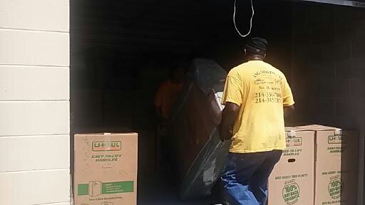 Two movers from Ang Moving Co loading items and boxes into a storage unit or truck in Dallas, TX