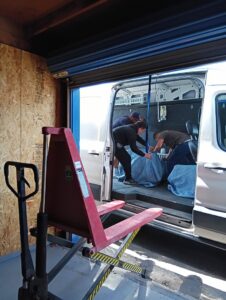 Three movers carefully loading wrapped items into the back of a white moving van for Rough Çutt Movers in San Diego, CA.