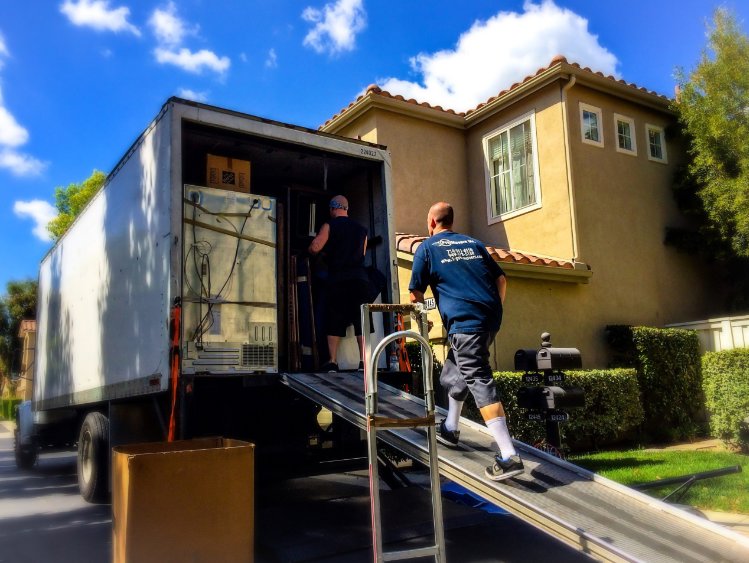 Two professional movers loading a large appliance into a moving truck up a ramp for Las Vegas Moving Pros LLC in Las Vegas, NV.