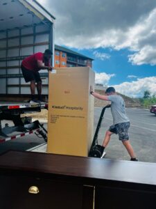 Two movers from The Knoxville Moving Co. loading a large box onto a moving truck using a hand truck in Knoxville, TN.