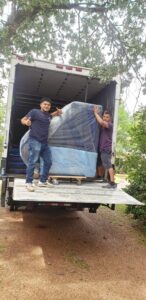 Two professional movers loading a large, wrapped item onto a moving truck for Emanuel Movers, Inc. in Houston, TX