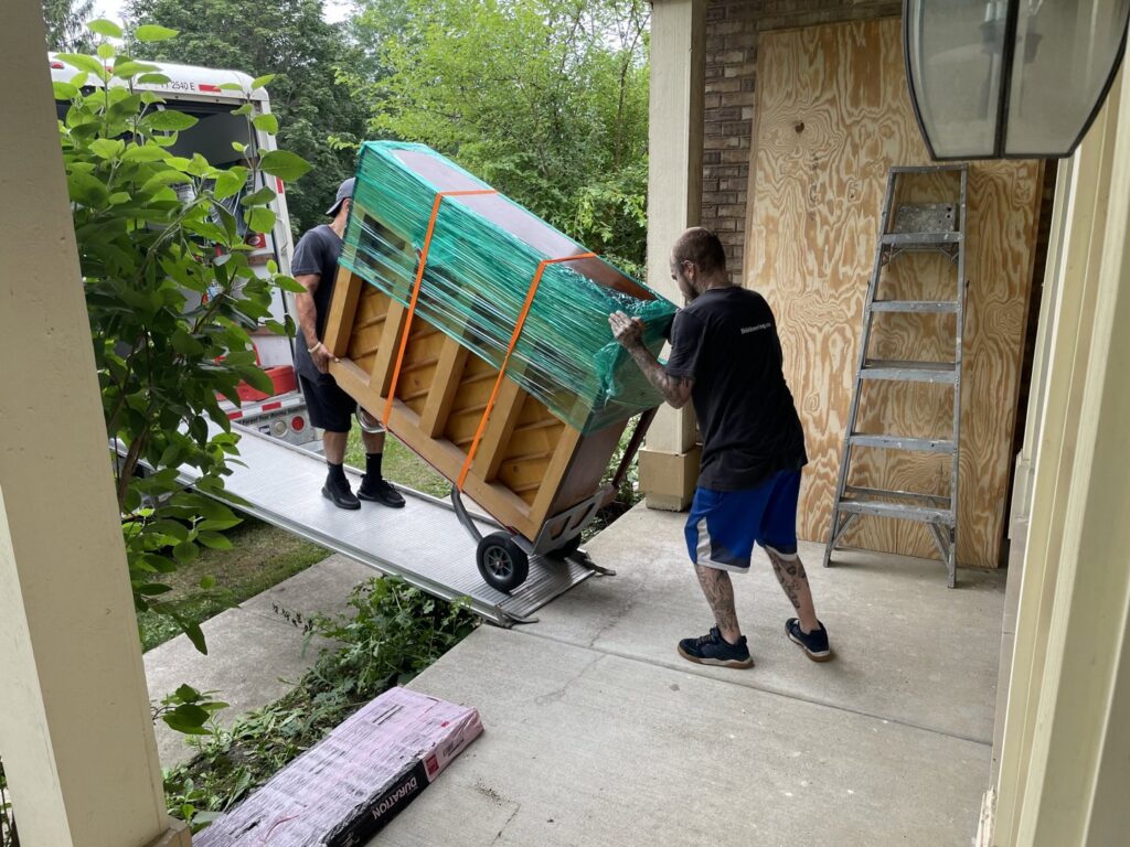 Shield Moving Services movers loading a wrapped piano into a moving truck using a ramp in Milwaukee, WI.