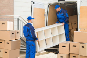 Two professional movers from Three Movers in Henderson, NV, carefully loading a shelving unit into a moving van.