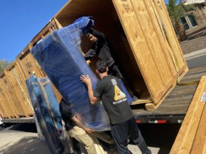 Muscular Moving Men & Storage movers carefully loading a wrapped sofa into a large wooden crate on a truck in Phoenix, AZ.