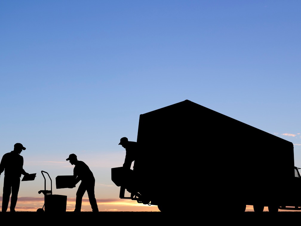 Professional movers loading boxes onto a truck at sunset for First Class Moving & Storage in Phoenix, AZ