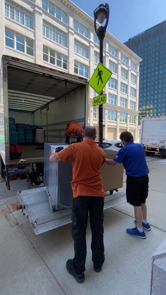 Movers loading large items onto a truck using a lift gate for Coakley Brothers & Brothers Interiors in Milwaukee, WI.