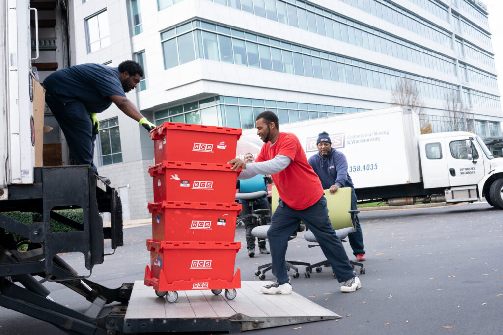 RCS Moving & Storage movers loading red bins and office chairs onto a moving truck with a lift gate during an office move in Richmond, VA.