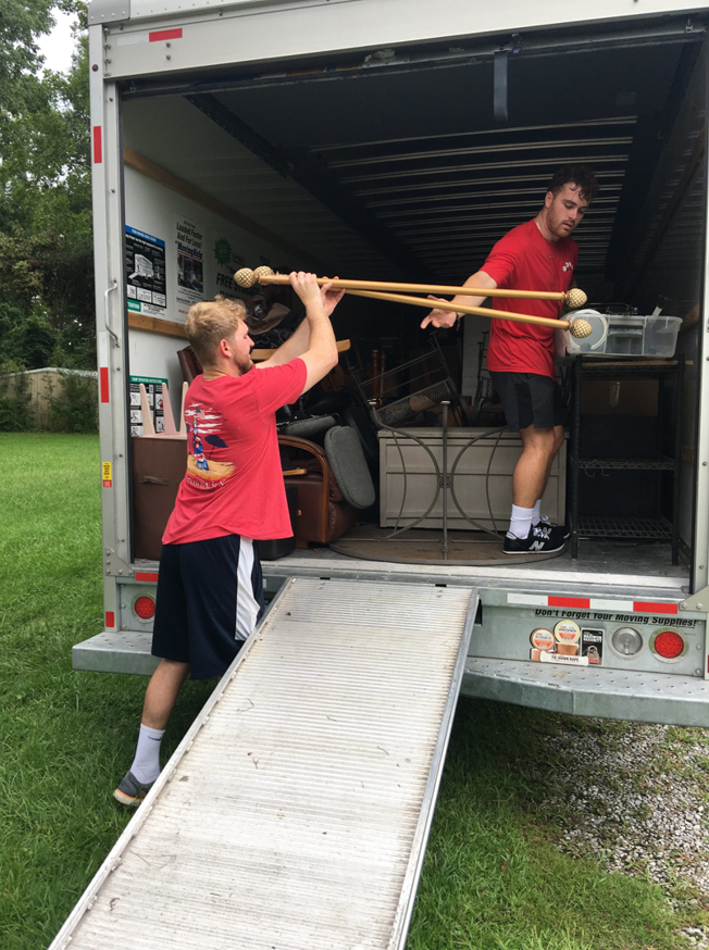 Two professional movers from Natural State Moving loading items onto a truck using a ramp in Conway, AR.