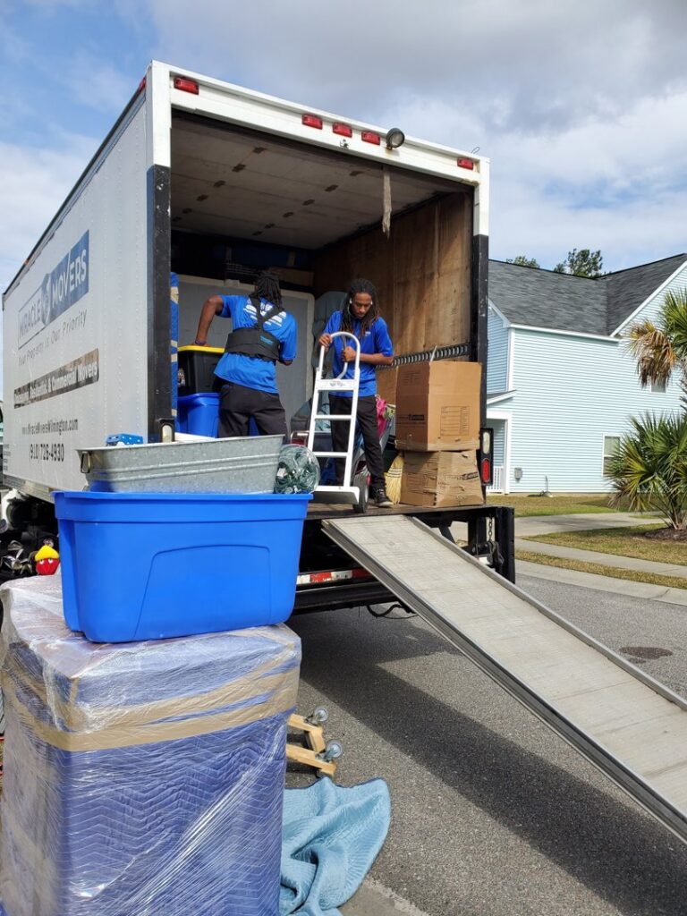 Two professional movers from Miracle Movers of Charleston, SC loading boxes and wrapped items onto a moving truck in Summerville, SC.