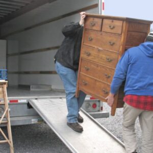 Two professional movers carefully loading a heavy wooden dresser down a ramp into a moving truck for Academy Movers in Gilbert, AZ.