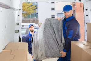 Two professional movers from Three Movers in Henderson, NV, loading a wrapped piece of furniture into the back of a moving van.