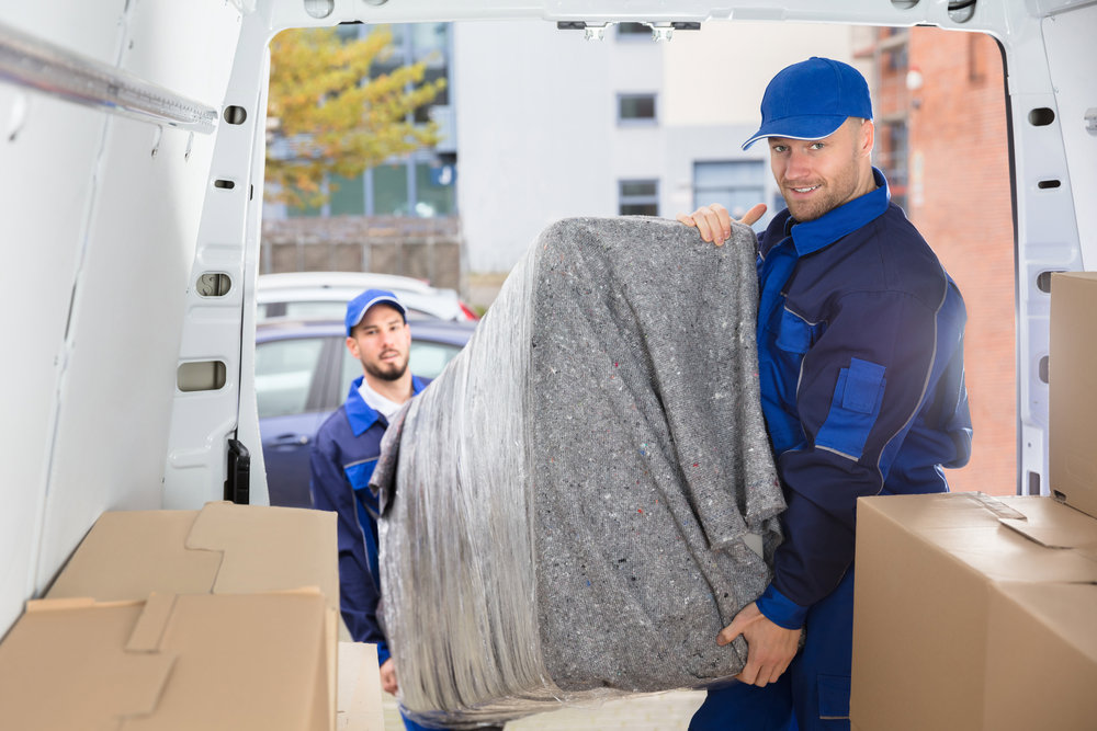 Two professional movers from Three Movers in Henderson, NV, loading a wrapped piece of furniture into the back of a moving van.