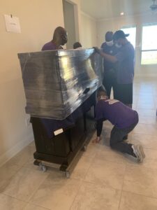 Several movers from Kingdom Men Movers in Houston, TX, carefully moving a large, wrapped cabinet on a dolly.