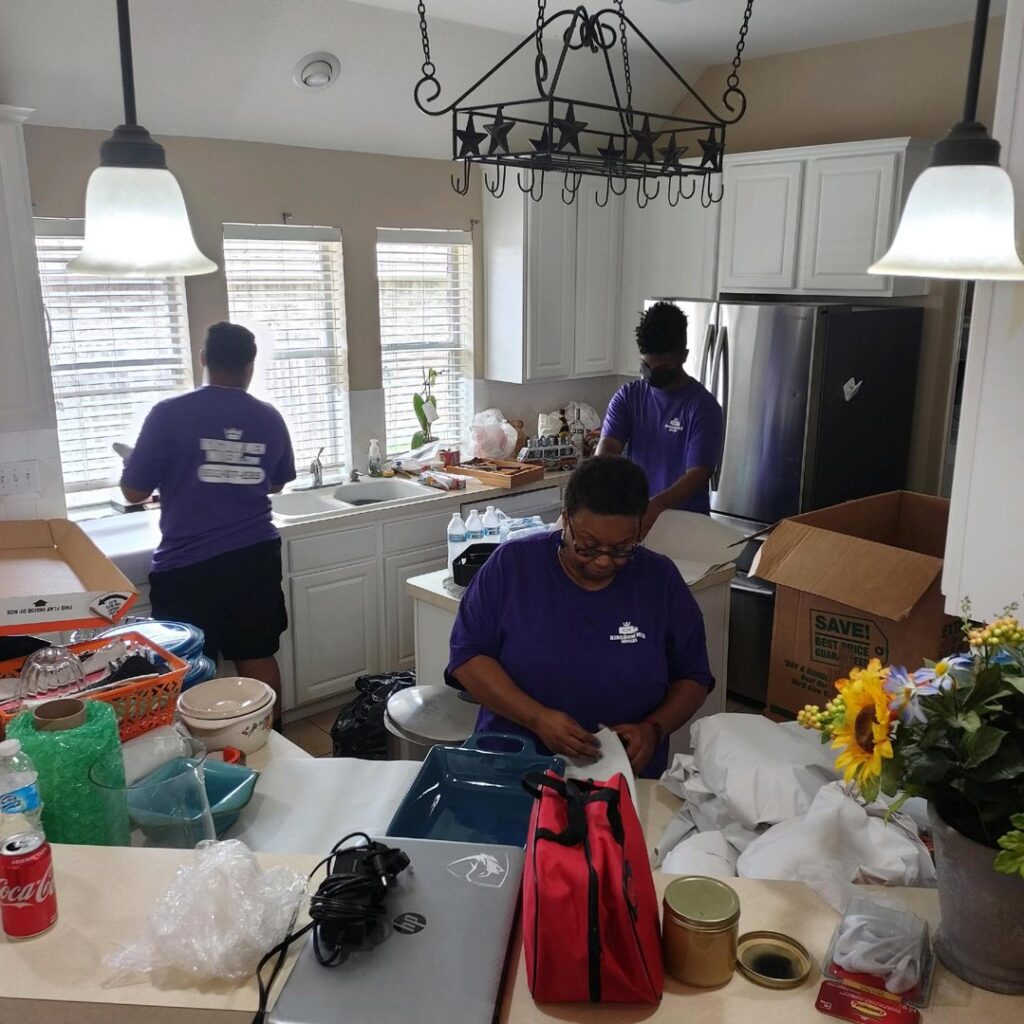 Three movers from Kingdom Men Movers in Houston, TX, diligently packing kitchen items into boxes during a residential move.