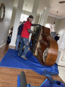 Professional movers carefully relocating a large piano inside a home, provided by Peroulas Moving and Storage in Knoxville, TN