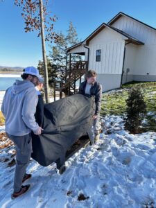 Two movers from The Knoxville Moving Co. relocating an outdoor grill in a snowy environment near a house in Knoxville, TN.