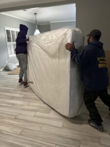 Two movers from Gifted Hands Moving & Storage in Collierville, TN, carefully relocating a large, wrapped mattress.