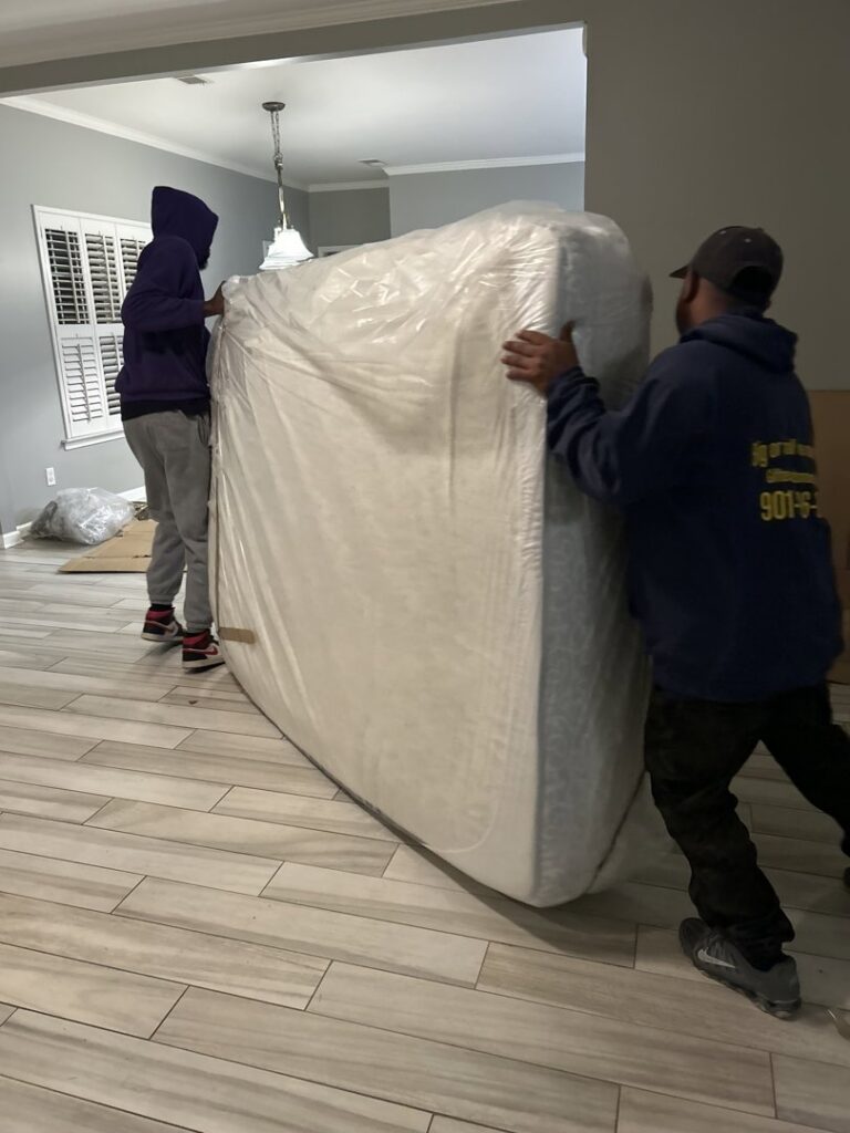 Two movers from Gifted Hands Moving & Storage in Collierville, TN, carefully relocating a large, wrapped mattress.