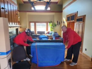Two professional movers from Joy Haul Professional Movers carefully relocating a wrapped sofa inside a home in Columbia City, IN.