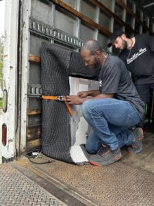 Two movers securing wrapped furniture inside a moving truck with straps for Rambling Man Logistics in Hildebran, NC.