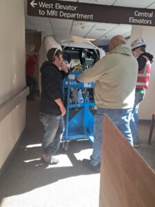 Professional movers transporting large medical equipment through a hallway, a service by Peroulas Moving and Storage in Knoxville, TN