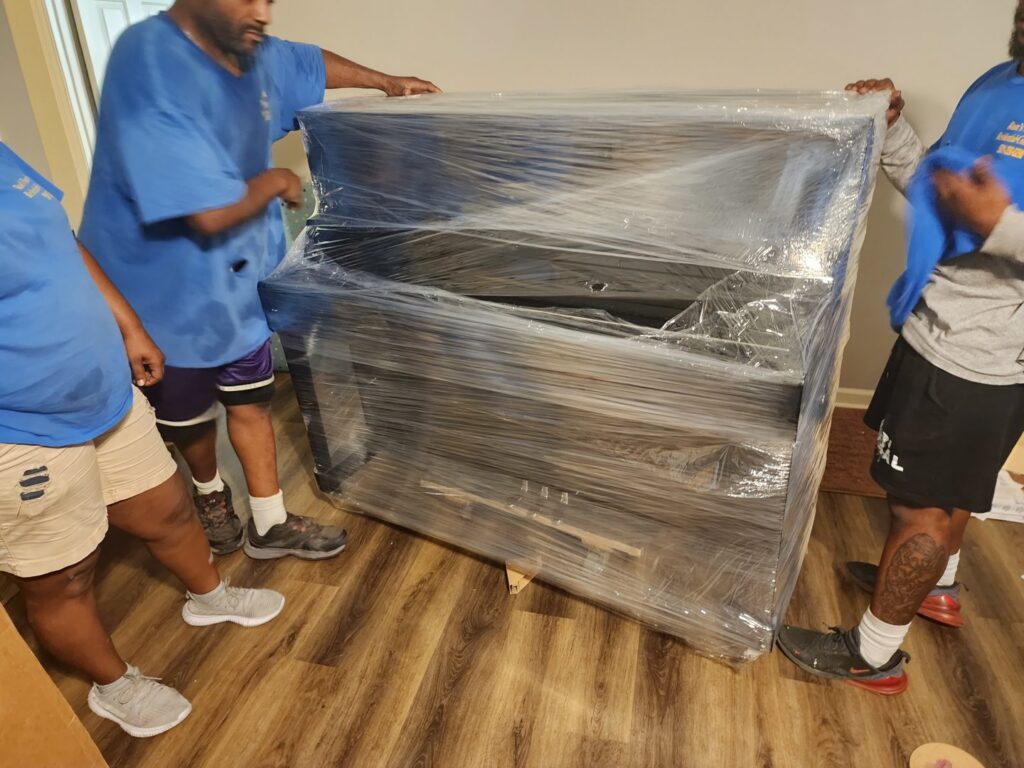 Three professional movers carefully transporting a large, wrapped piano for Ron's Moving in Little Rock, AR.