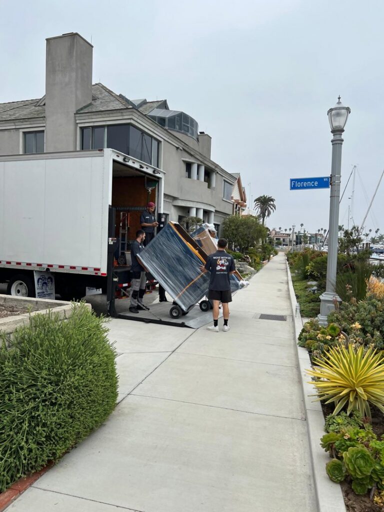 Professional movers carefully unloading a large, wrapped item from a moving truck using a lift gate for All Way Moving in Washington, PA.